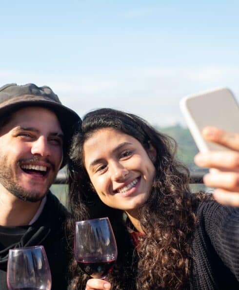 Jeune homme et jeune femme prenant un selfie, un verre de vin à la main